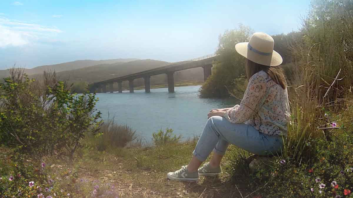 Jovem mulher com chapéu de palha sentada na margem do rio Salas em Tourém