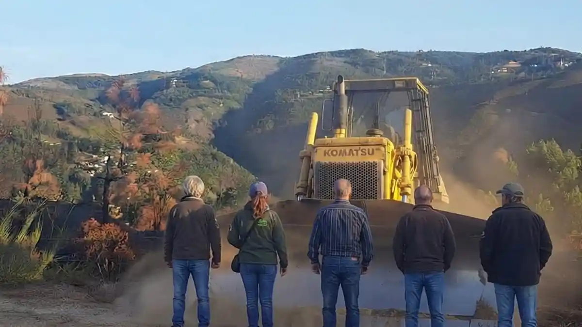 Cinco pessoas de costas a fazer barreira em frente a uma grande escavadora bulldozer amarela numa montanha do Barroso