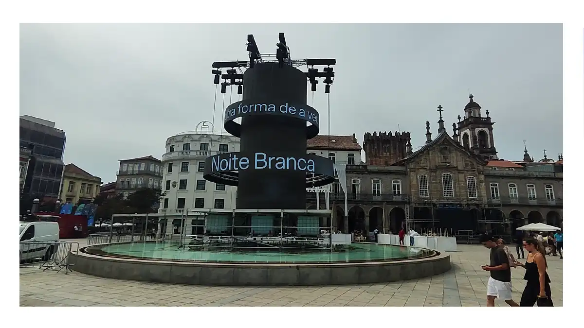 Estrutura cilíndrica preta com painéis eletrónicos da Noite Branca instalada no chafariz da Praça da República em Braga, em frente ao edifício da Arcada.