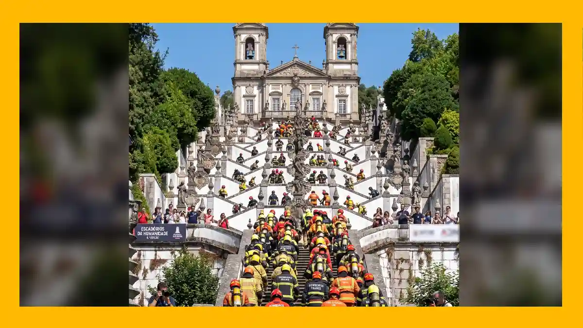 Cartaz com moldura amarela mostrando os Escadórios do Bom Jesus do Monte em Braga repletos de bombeiros fardados a subir os degraus em direção ao santuário, com efeito de desfoque nas laterais.